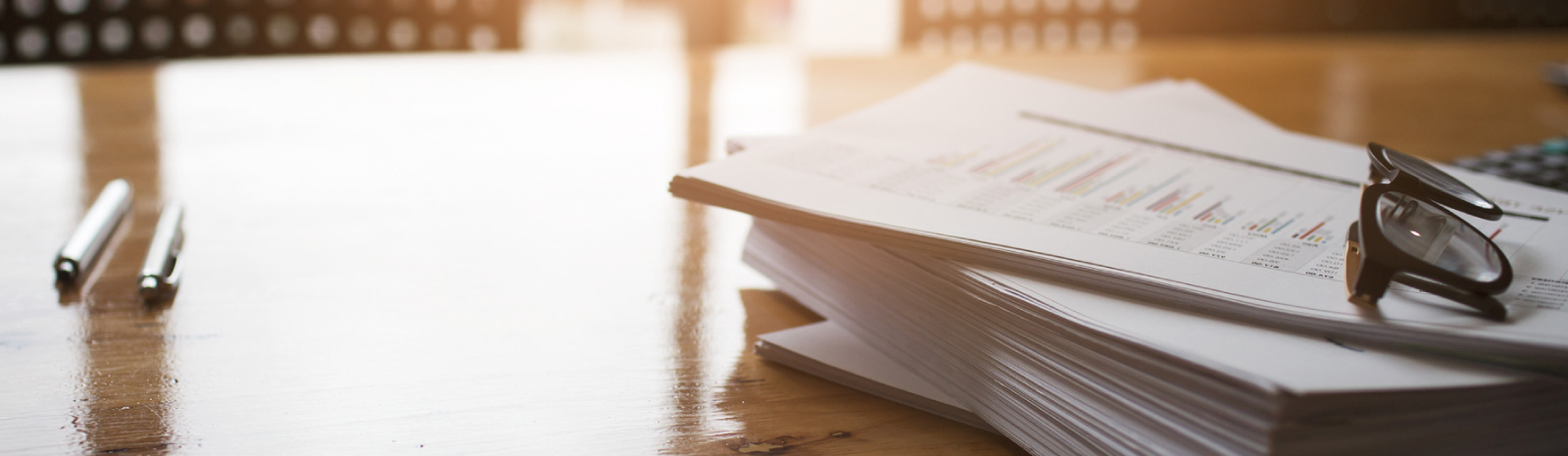 A stack of papers on a desk with eyeglasses