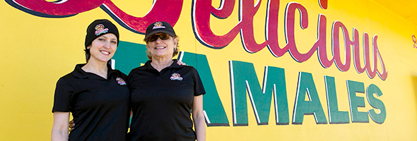 two women in front of delicious tamales sign